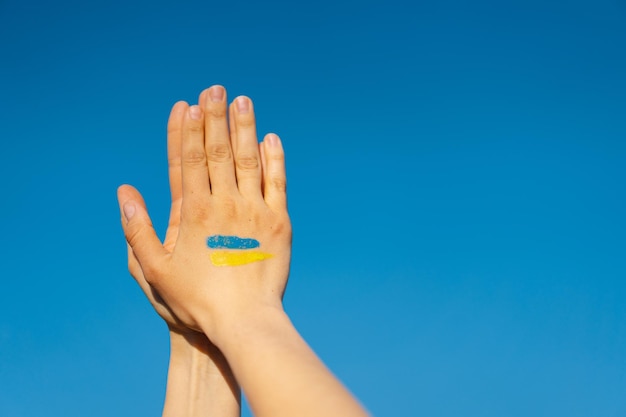 Mains de femme avec le symbole du drapeau ukrainien priant pour arrêter la guerre en Ukraine