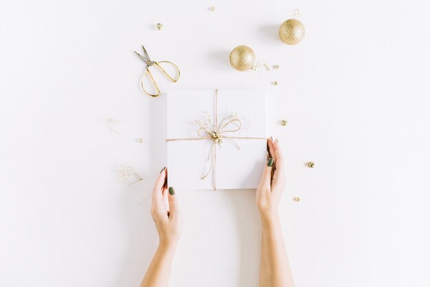 Mains de femme tenant une boîte cadeau blanche avec archet. Mise à plat de Noël, vue de dessus