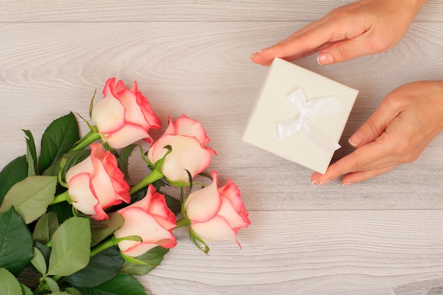 Mains de femme tenant une boîte-cadeau sur fond de bois gris avec de belles roses. Concept de donner un cadeau en vacances. Vue de dessus.