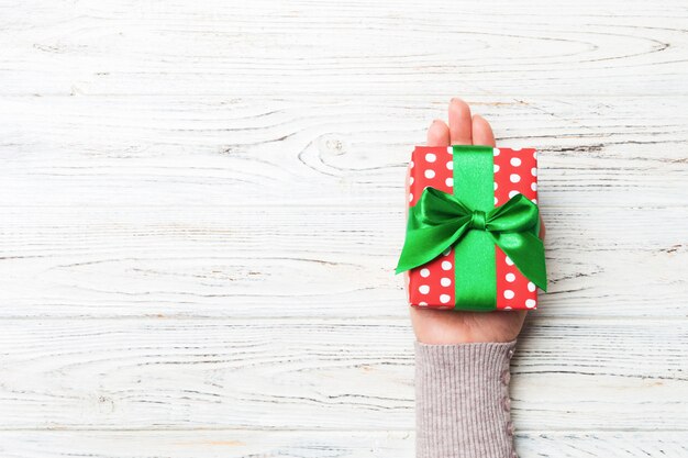 Mains de la femme tenant une boîte cadeau rayée avec un ruban de couleur sur du bois rustique blanc