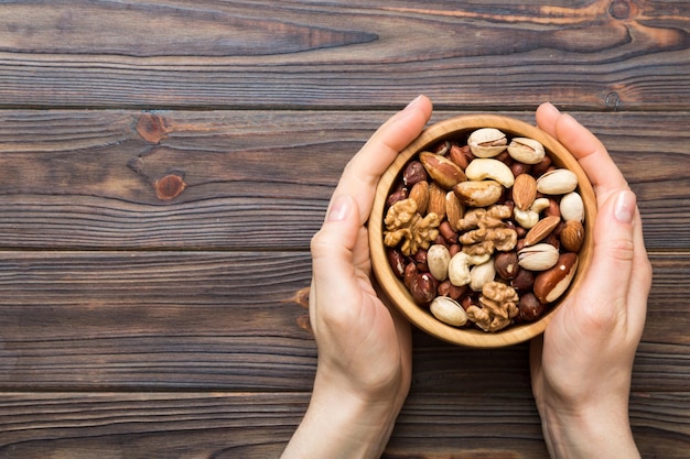 Mains de femme tenant un bol en bois avec des noix mélangées Noix pistaches amandes noisettes et noix de cajou Aliments sains et collations Collations végétariennes de différentes noix