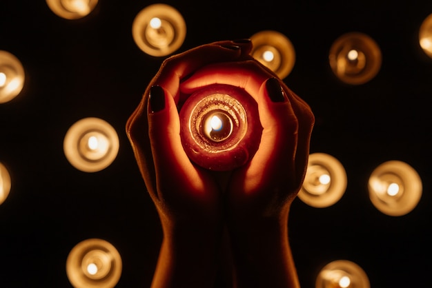 Mains de femme tenant une bougie allumée. De nombreuses flammes de bougies brillent. Fermer.