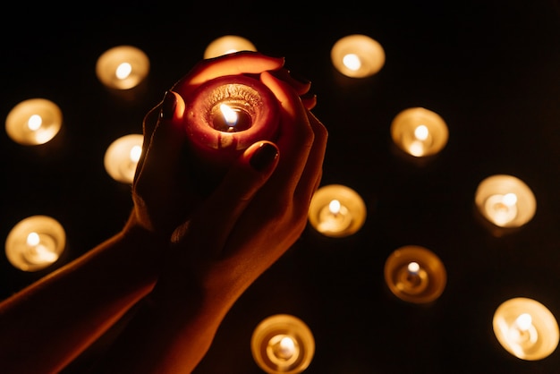 Mains de femme tenant une bougie allumée. De nombreuses flammes de bougies brillent. Fermer.