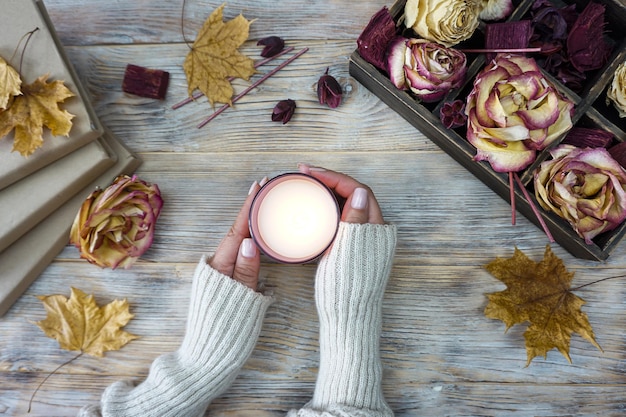 Les mains d'une femme tenant une bougie avec des feuilles d'automne sur la table.