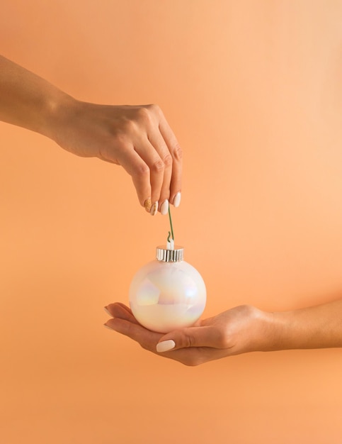 Mains de femme tenant une boule de Noël brillante blanche sur fond orange pastel Concept de vacances minimal Bonne année