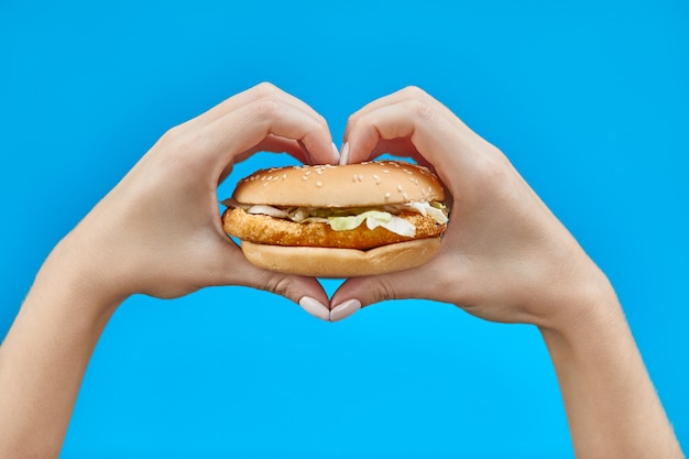 Mains de femme tenant un burger sur un bleu