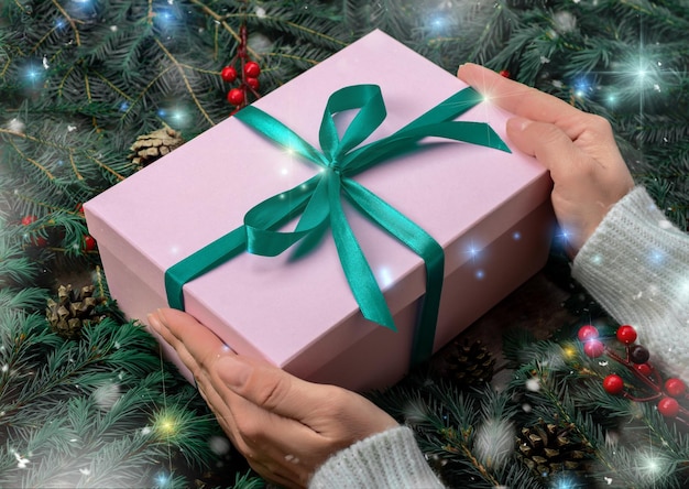 Mains de femme tenant un cadeau de Noël ou une boîte cadeau décorée de sapins et de lumières de Noël Préparation pour les vacances et la célébration Mains féminines tenant un cadeau ou une boîte cadeau