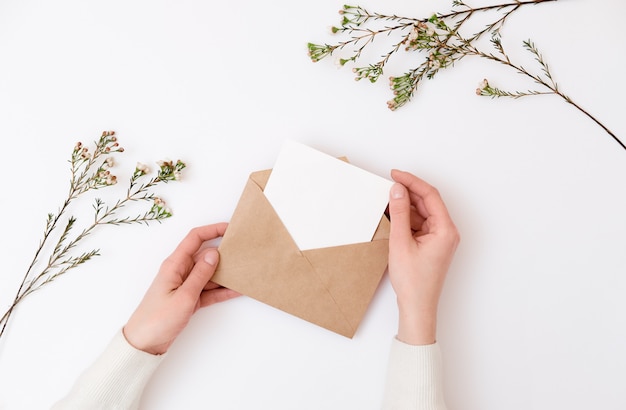 Mains de femme tenant une enveloppe kraft avec carte d&#39;invitation de mariage vierge