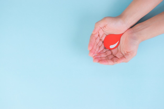 Mains de femme tenant une goutte de sang rouge