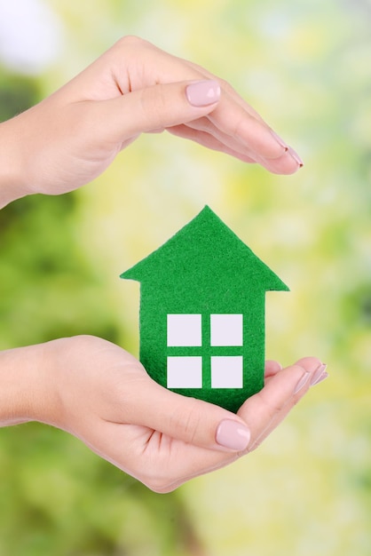 Mains de femme tenant une maison en papier sur fond clair