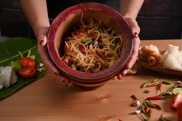 Mains de femme tenant un mortier avec salade de papaye concept de cuisine thaïlandaise