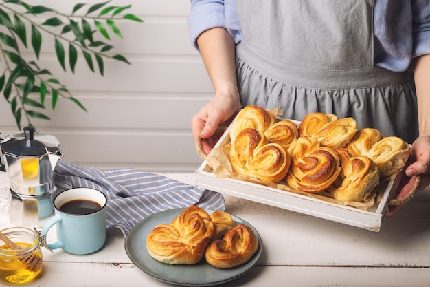 Mains de femme tenant un plateau en bois blanc avec des petits pains faits maison.