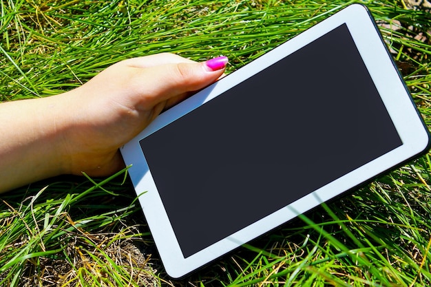 Mains de femme tenant une tablette blanche avec un écran vierge sur un gr vert