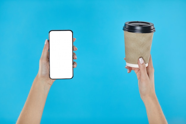 Mains de femme tenant la tasse de papier café et smartphone sur un bleu.