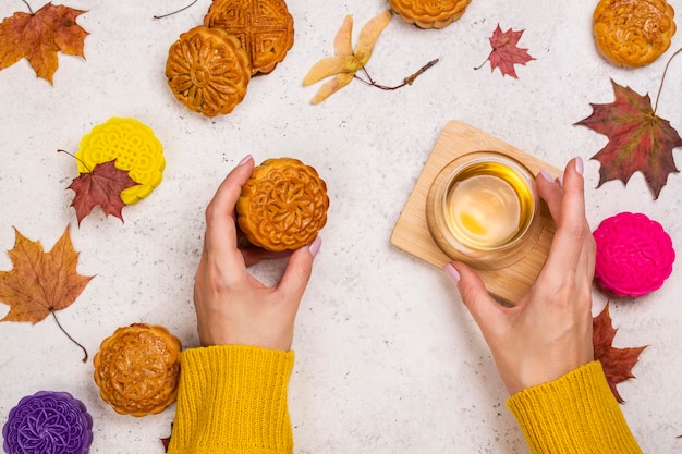 Les mains de la femme tenant une tasse de thé vert et un gâteau de lune yuebing. Gâteau yuebing chinois traditionnel - gâteau de lune et feuille d'érable sur fond de pierre claire. Fond de festival de mi-automne