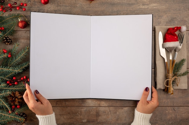 Les mains d'une femme tiennent la maquette du menu de Noël Maquette du menu de la recette de Noël sur du bois rustique