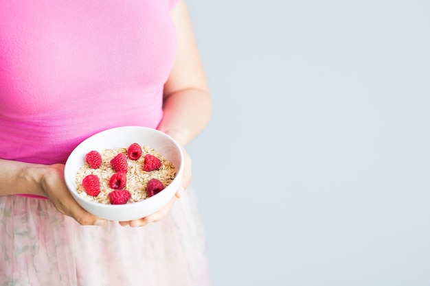 Les mains de la femme tiennent un petit-déjeuner sain et naturel, des flocons d'avoine et des framboises dans un bol.