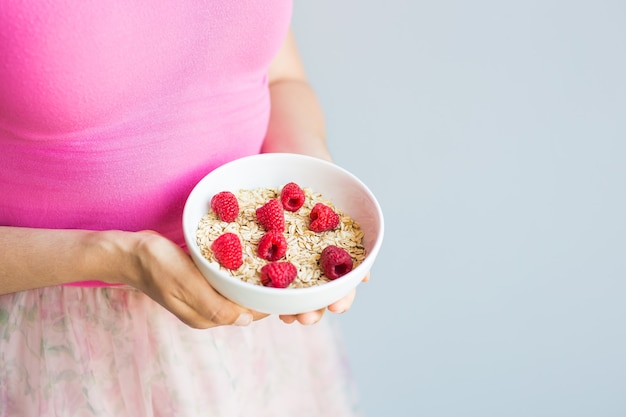 Les mains de la femme tiennent un petit-déjeuner sain et naturel, des flocons d'avoine et des framboises dans un bol.