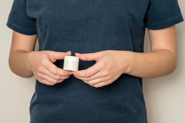 Les mains d'une femme tiennent un pot en plastique contenant un produit cosmétique