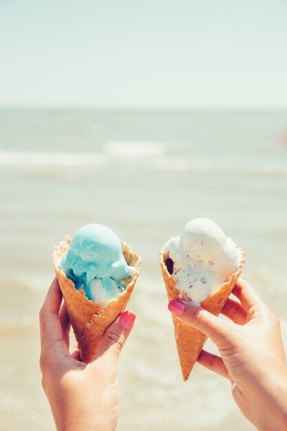 Les mains de la femme tient deux glaces sur la mer