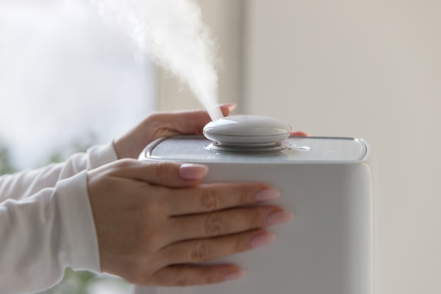 Mains de femme touchant et utilisant un diffuseur d'huile d'arôme sur la table à la maison, vapeur de l'humidificateur d'air