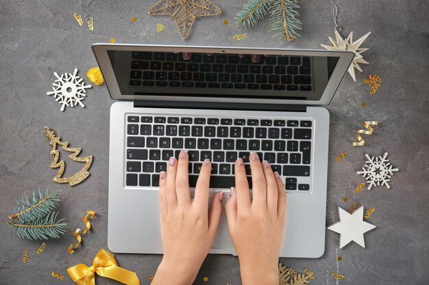 Mains de femme utilisant un ordinateur portable et des décorations de Noël sur fond gris