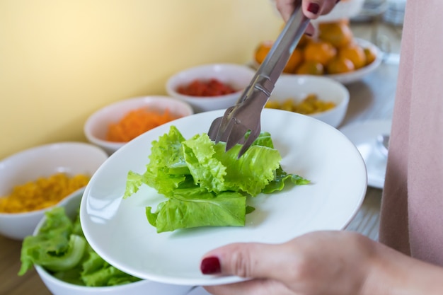 Les mains de la femme utilisent un légume vert avec une pince blanche sur la plaque blanche.