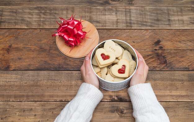 Les mains des femmes avec une boîte ouverte de biscuits en forme de cœur sur une base en bois. Concept Saint-Valentin, fête des mères, anniversaire.