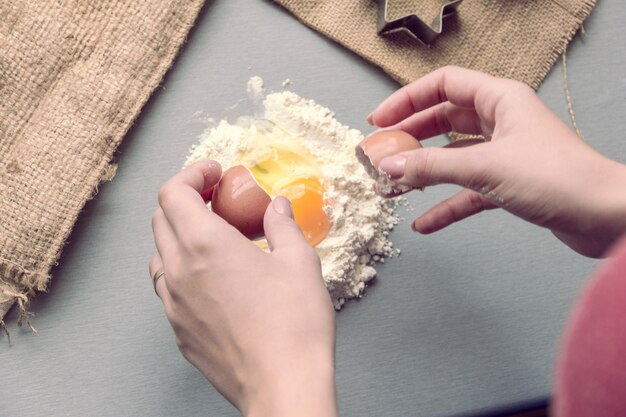 Les mains des femmes cassent un œuf de poule en farine