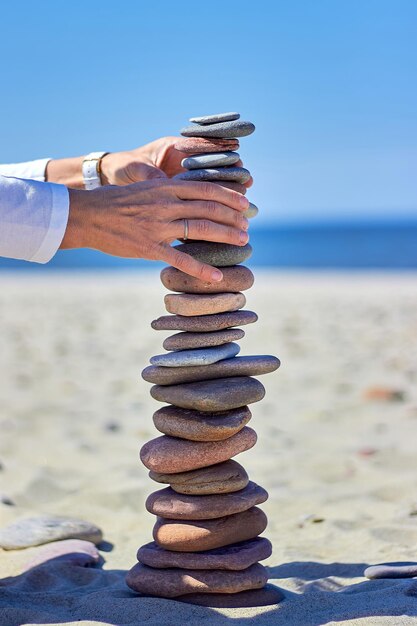 Les mains des femmes construisent un haut cairn sur une plage de sable