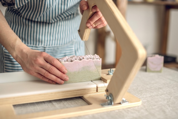 Les mains des femmes coupent du savon naturel fait maison sur un coupe-bois professionnel Un moyen d'hygiène écologique