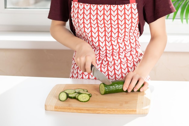 Les mains des femmes coupent des légumes sur une planche de bois dans la cuisine Régime alimentaire sain