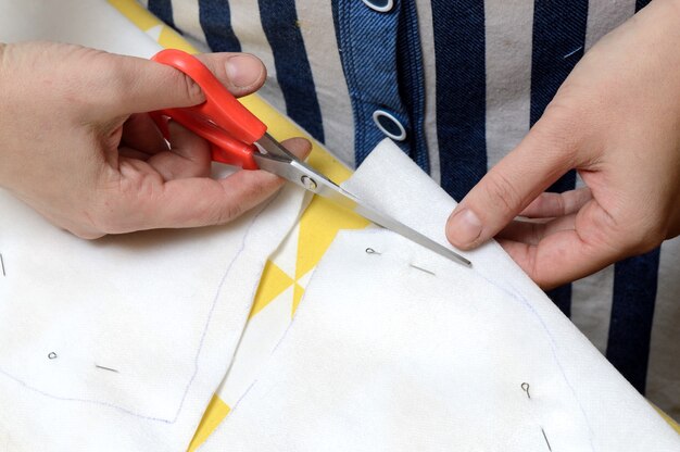 Les mains des femmes coupent le tissu avec des ciseaux selon le motif sur la table.