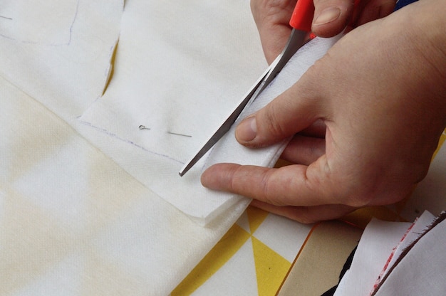 Les mains des femmes coupent le tissu avec des ciseaux selon le motif sur la table.