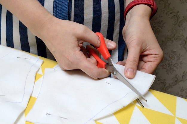 Les mains des femmes coupent le tissu avec des ciseaux selon le motif sur la table.