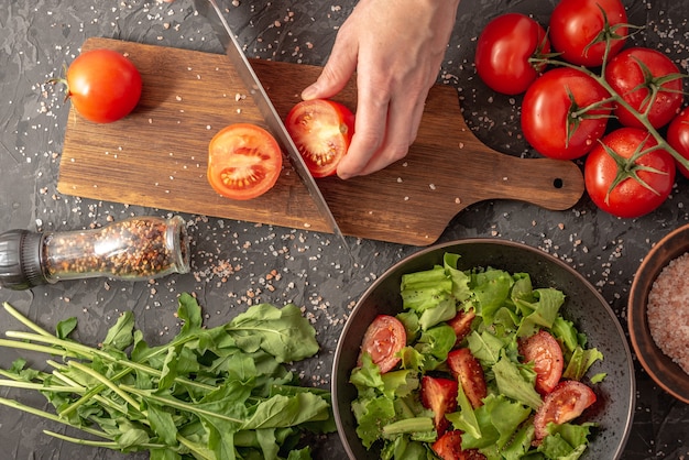 Les mains des femmes coupent une tomate mûre pour cuisiner une salade de légumes avec des tomates et de la roquette