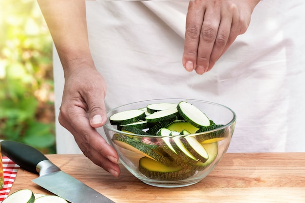 Les mains des femmes courgettes en tranches de sel dans un bol en verre