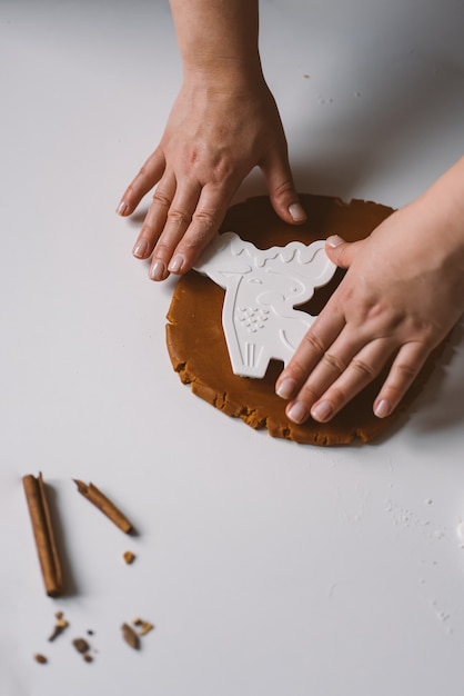 Les mains des femmes avec un cutter en forme de cerf découpent des biscuits en pain d'épice de la pâte