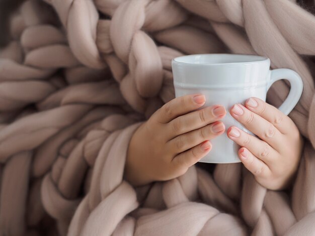 Les mains des femmes dans une couverture chaude en laine mérinos avec une tasse de café