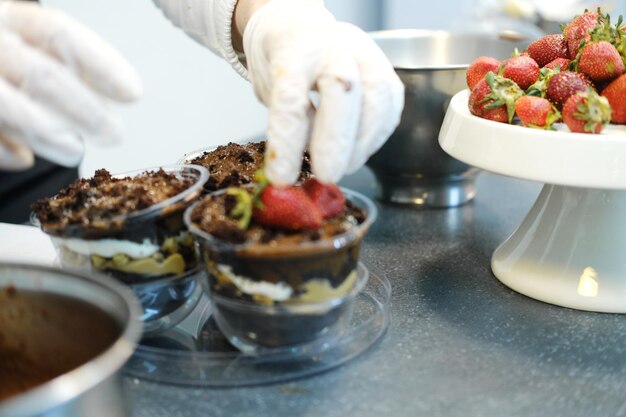 Les mains des femmes dans des gants blancs décorent un dessert au chocolat avec des fraises fraîches photo horizontale