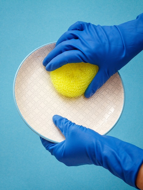 Photo mains de femmes dans des gants de protection bleus avec plaque et éponge jaune. concept de lavage et de nettoyage.