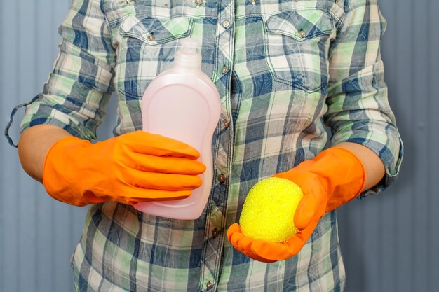 Les mains des femmes dans des gants de protection avec une bouteille de liquide vaisselle