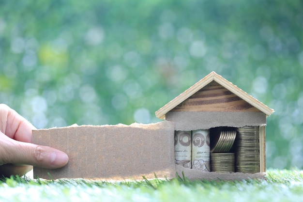 Les mains des femmes déchirent une feuille de papier marron et de l'argent dans une maison modèle sur fond vert naturelInvestissement d'affaires et concept immobilier