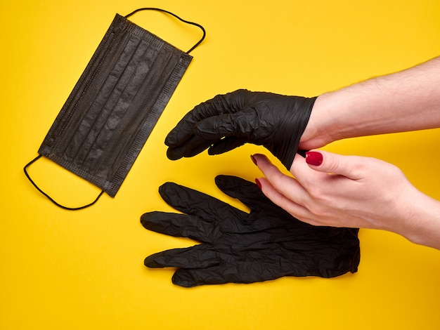 Les mains des femmes décollent des gants noirs avec un masque noir jaune