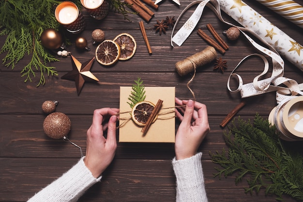 Les mains des femmes décorent une boîte-cadeau de noël avec des décorations naturelles écologiques hobby créatif bricolage