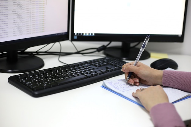 Les mains des femmes écrivent dans un cahier contre un écran d'ordinateur