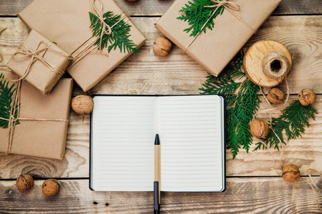 Les mains des femmes écrivent dans un cahier avec un stylo. Boîtes d'emballage en papier kraft sur fond bois.Matériau respectueux de l'environnement. Artisanat d'art fait à la main. Le concept de Noël et du nouvel an.