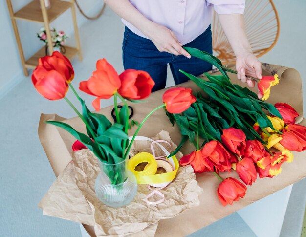 Les mains des femmes emballent un bouquet festif dans du papier d'emballage Le fleuriste fait un assemblage avec des tulipes rouges dans l'atelier Une femme au travail petite entreprise ou passe-temps