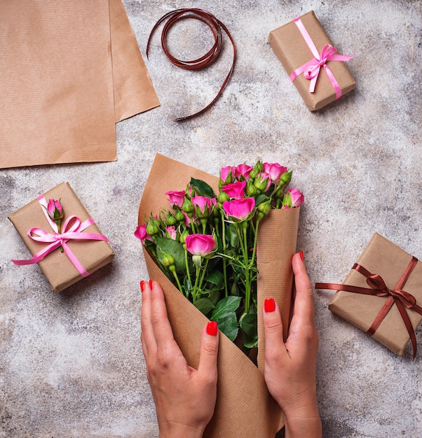 Des mains de femmes enveloppent un bouquet de roses en papier