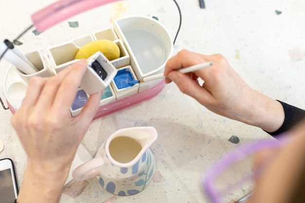 Les mains des femmes mélangent de la peinture pour colorer un pot à lait en céramique dans l'atelier.